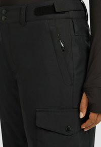 Zwarte outdoorbroek met een gladde textuur, twee knoopsluitingen, een cargozak en een klittenbandriem. Bevat een subtiele merklabel aan de zijkant.