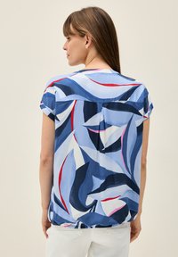 Blusa a maniche corte in tessuto azzurro chiaro con motivo a foglie in blu navy, bianco e rosso. Schiena drappeggiata e vestibilità comoda con dettaglio a pieghe.