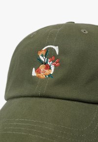 Gorra de algodón color caqui con diseño floral bordado en naranja, amarillo y verde en la parte frontal; forma estructurada con costuras visibles.
