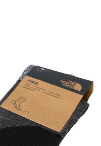 Calcetines de crew grises en una etiqueta de cartón etiquetada "HIKE" de The North Face, con tamaño "M" e instrucciones de cuidado. Detalle de la tela texturizada visible.