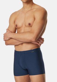 Marinblå boxershorts i ribbat material med elastiskt midjeband och en sydd logotypdetalj på vänster framsida.
