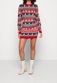 Abito maglione a righe rosso e nero con motivi natalizi e fiocchi di neve, in tessuto lavorato a maglia con polsini e orlo a coste. Indossato con stivali crema.