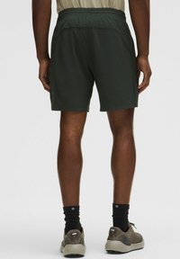 Pantalones cortos de deporte de color verde oscuro con una cinturilla elástica, textura suave y un diseño hasta la rodilla, combinados con zapatillas de tonos neutros y calcetines negros.