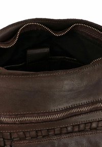 Binnenkant van een bruine leren tas met een ritsvak, met een gestructureerde afwerking en contrasterende stiksels. Donkere stoffen voering zichtbaar.