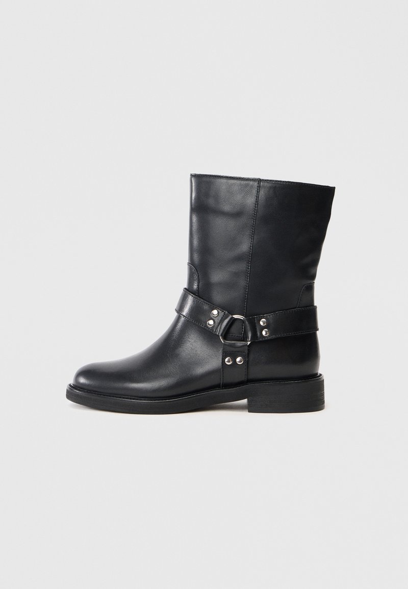 Schwarze Lederstiefelette mit flachem Absatz, die mit einem Schnallenriemen und metallischen Akzenten verziert ist, glatte Textur und strukturiertes Design.