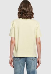 Ljusgul bomullströja med avslappnad passform, korta ärmar och rundad halsringning, tillsammans med blekta blå jeans. Slät textur.