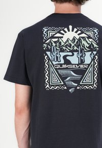Navy T-shirt with graphic print featuring mountains, cacti, and a river, accented by geometric patterns in light blue and green tones.