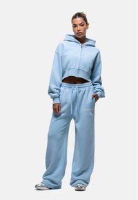 Felpa cropped azzurra chiara con zip frontale, abbinata a pantaloni della tuta larghi coordinati con vita elasticizzata e dettaglio del logo.