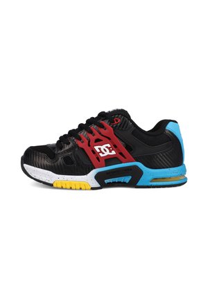 Chaussure de sport noire avec un support latéral rouge, un talon bleu, une semelle jaune et blanche mouchetée, et un logo DC blanc sur le côté.