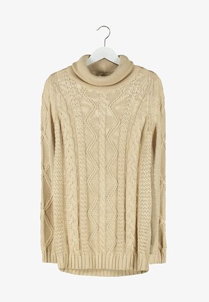 Pull oversized en maille torsadée beige avec col montant, associé à un jean skinny noir et des bottines noires avec des brides à boucles.