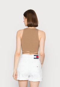 Top cropped canelado bege com decote alto, combinado com calções de ganga brancos com as bainhas dobradas e um emblema na parte de trás.