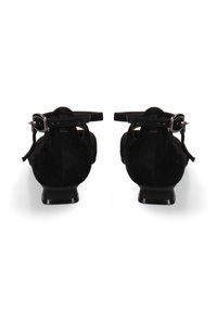Zwarte suède damesschoenen met enkelbandjes en zilveren gespen, lage hakken, bekeken van achteren op een witte achtergrond.