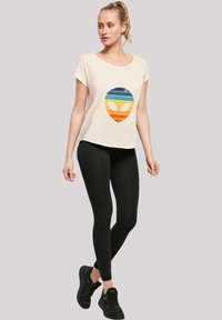 Cream T-shirt with a multicolored alien graphic, paired with black leggings and black sneakers. Soft fabric, relaxed fit, short sleeves.