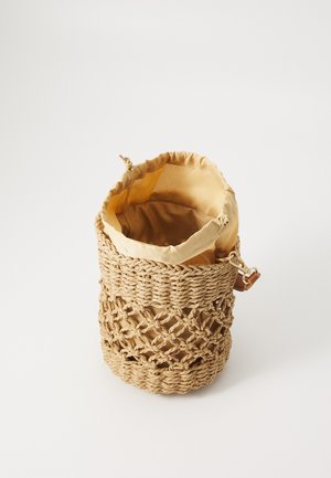 Flettet strå bucket taske med beige stofforing, snøring lukkemekanisme og aftagelig læderstrop med spænde på hvid baggrund.