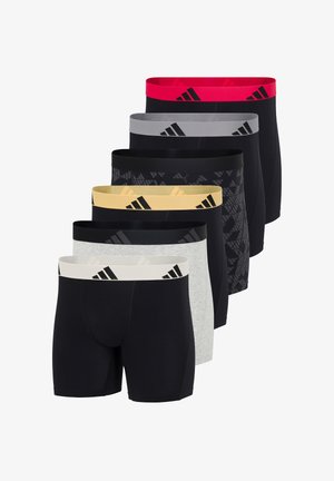En bar overkrop mand, stående barfodet iført sorte boxershorts med en gul linning med sorte diagonale striber.