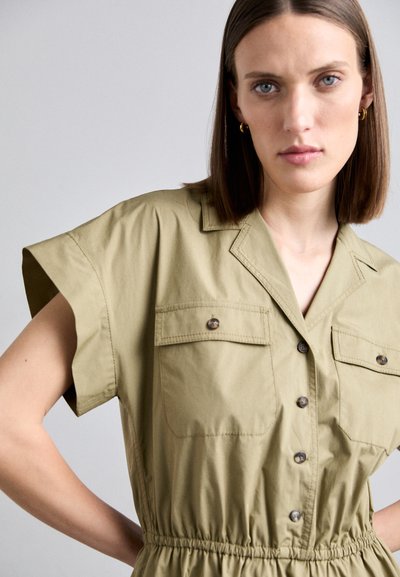 Khaki Kurzarm-Overall mit einem kragenlosen Ausschnitt, zwei Brusttaschen und einem elastischen Bund. Haptisches, leichtes Gewebe mit Knöpfen.