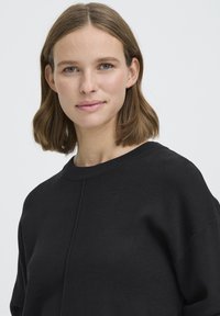 Must varrukateta dressipluus, pehme tekstuuri, soonikkoes mansettide ja minimalistliku disainiga. Kerge materjaliga ja lõdva istuvusega.