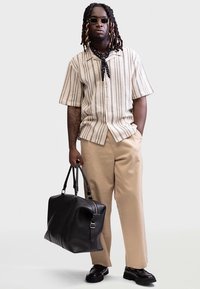 Beige striped short-sleeve shirt, khaki trousers, black leather bag, and dark shoes. Accessories include sunglasses and a patterned scarf.