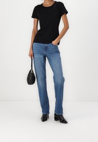 Camiseta negra de manga corta con escote adornado, combinada con jeans rectos de color azul claro y botines negros de tacón, sosteniendo un bolso negro.