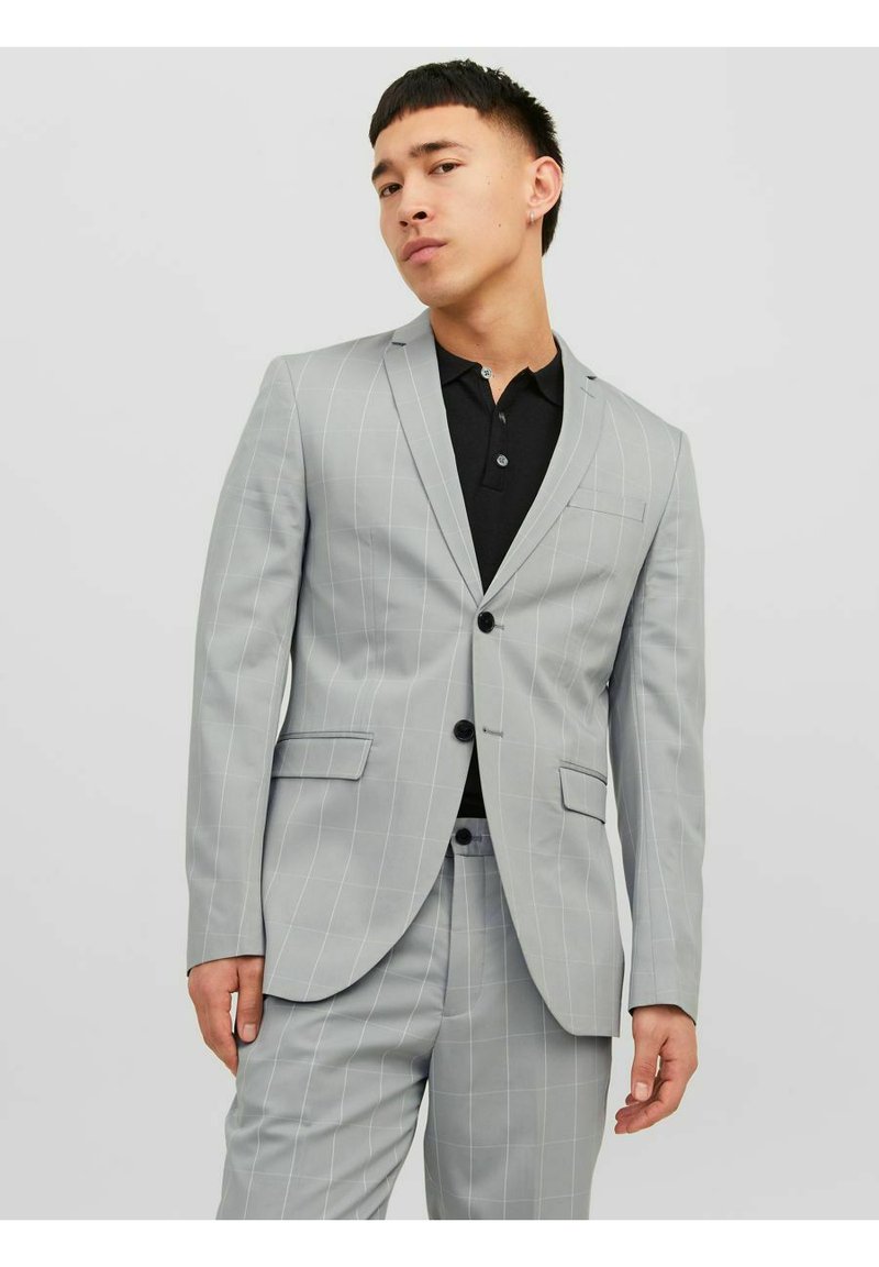 Costume rayé gris avec une veste à un bouton et un pantalon à devant plat. Présente des revers crantés et des poches latérales, porté sur un polo noir.
