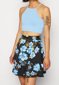 Light blue halter crop top paired with a black skirt featuring a layered design and large blue florals with green and red accents.