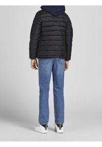 Svart puffjacka med sömmade paneler, marinblå huva, buren över blå denimjeans och vita sneakers med svarta detaljer på hälarna.