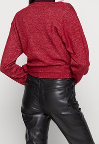 Roter, strukturierter Pullover mit langen Ärmeln und lockerem Sitz, kombiniert mit schwarzen Kunstlederhosen mit Gesäßtaschen und Nahtdetails.