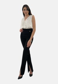 Pantaloni neri con spacchi laterali, design a vita alta e un accento in bottone dorato. Abbinati a un top bianco senza maniche realizzato in tessuto liscio.