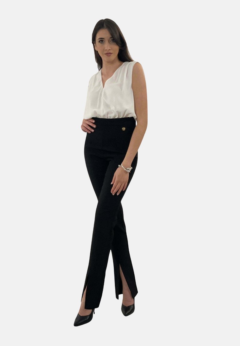 Pantaloni neri con spacchi laterali, design a vita alta e un accento in bottone dorato. Abbinati a un top bianco senza maniche realizzato in tessuto liscio.