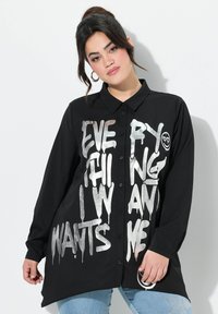 Zwarte button-up shirt met grote, zilveren druipende tekst, "ALLES WAT IK WIL." Lange mouwen, ontspannen pasvorm, met een afgeronde zoom.
