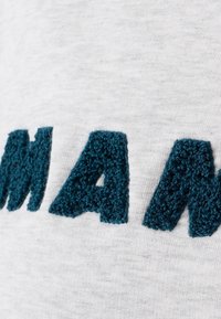 Tela gris con un texto turquesa texturizado y en relieve. Las letras tienen un aspecto borroso, contrastando con el fondo suave.