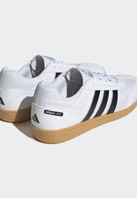 Baskets de sport blanches avec tige en mesh, design à trois bandes noires et semelle en caoutchouc couleur gomme. Étiquette "SPEZIAL LIGHT" au niveau du talon.