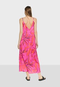 Floral print maxi dress in bright pink, featuring a v-back, thin straps, and smooth fabric with orange and blue leaf patterns.