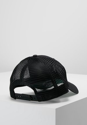 Zwarte mesh truckerpet met verstelbare snapbackriem, gebogen klep, geplaatst op een wit hoekig oppervlak tegen een grijze achtergrond.