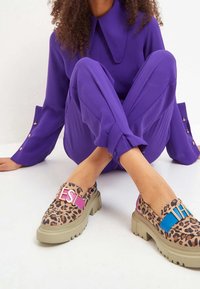 Scarpe slip-on con stampa leopardata e suole beige spesse. Presentano bande di accentuazione colorate in rosa e blu, con le lettere "ES" e "HI."