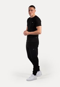Sort t-shirt med kort ærme og et lille logo, parret med sorte joggers med sidelommer og hvide sneakers.