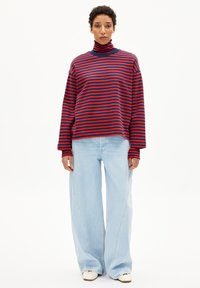 Rood en blauw gestreepte turtleneck trui met lange mouwen, gecombineerd met lichtblauwe wijde jeans met een relaxte pasvorm en minimale details.
