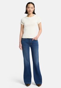 Kremowy t-shirt z krótkim rękawem w połączeniu z wysokim stanem, dzwonowatymi niebieskimi dżinsami. Dżinsy mają kieszenie i akcenty w zwierzęcy wzór na dole nogawek.