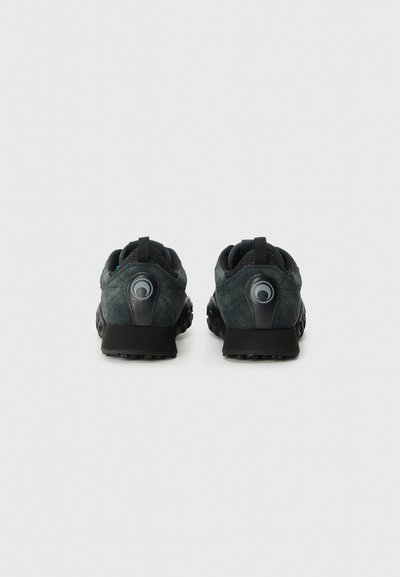 Black and dark teal athletic shoes with a textured suede upper, rounded heel, and circular accent detail on the rear.