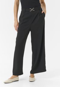 Schwarze, weit geschnittene Hose mit hoher Taille, ausgestattet mit einem metallischen, runden Schnallen-Gürtel und seitlichen Taschen. Weiches, leichtes Material.
