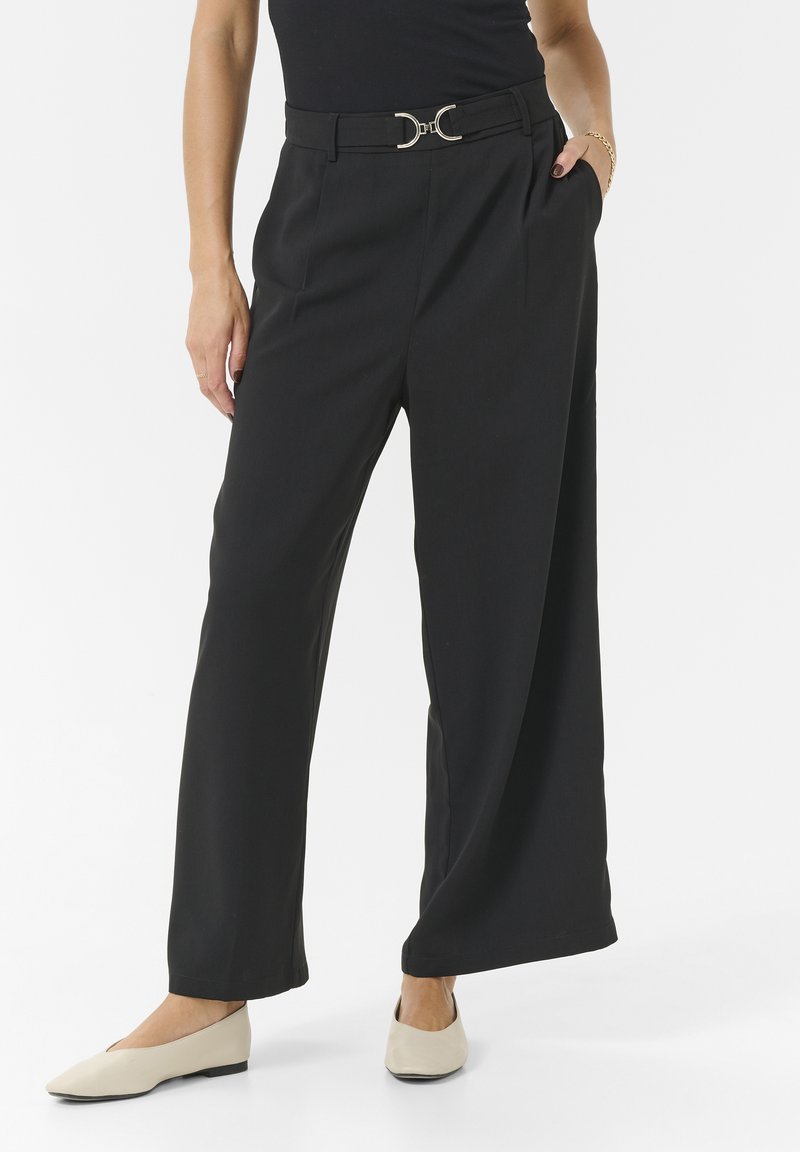 Schwarze, weit geschnittene Hose mit hoher Taille, ausgestattet mit einem metallischen, runden Schnallen-Gürtel und seitlichen Taschen. Weiches, leichtes Material.