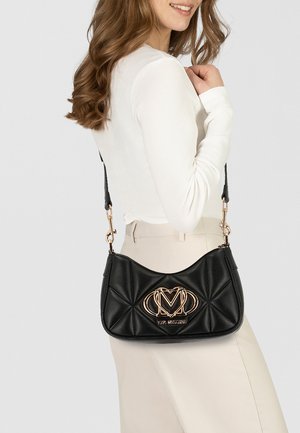Schwarze Handtasche aus weichem, gesteppte Leder, mit einem goldenen Logoakzent und einem abnehmbaren Tragegurt, in einer eleganten, geschwungenen Form.
