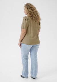 Blouse à manches courtes vert olive avec épaules bouffantes, en tissu texturé, associée à un jean évasé bleu clair et des ballerines noires.