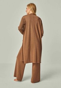 Brauner Strickcardigan mit langem Rückenschlitz, kombiniert mit passenden weit geschnittenen Hosen. Weiche Textur, lässige Passform und minimalistisches Design.