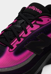 Gros plan sur une chaussure New Balance noire et rose vif avec des lacets noirs et le texte « ellipse » sur la languette.