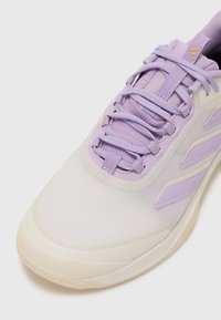 Scarpa sportiva di colore lilla chiaro con tomaia in rete, lacci piatti e tre strisce laterali testurizzate. Sole in gomma crema con un design elegante e minimalista.