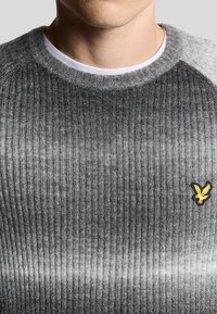 Grauer gerippter Pullover mit einem verlaufenden Design, das ein gelbes gesticktes Logo auf der Brust und einen Rundhalsausschnitt aufweist. Weicher Stoff.