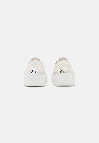 Witte canvas schoenen met een dikke witte zool, voorzien van zilveren metalen accenten bij de hiel en elastische banden voor een instapstijl.