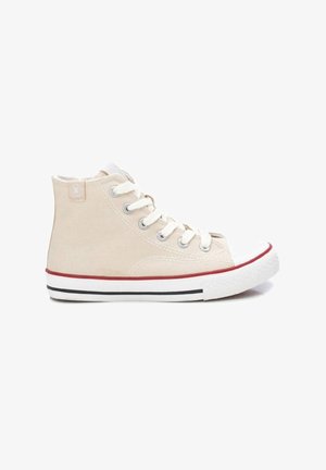 Zapatilla alta de lona beige con puntera de goma blanca, suela a rayas rojas y negras, y ojales plateados con cordones.