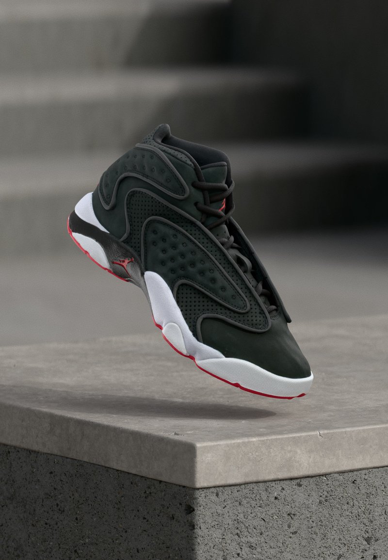 Μαύρο και κόκκινο sneaker υψηλής κοπής με λευκή σόλα αιωρείται πάνω από μια τσιμεντένια άκρη με θολές σκάλες στο παρασκήνιο.